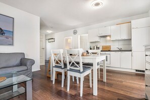 A modern kitchen with white cabinets, a dining area with a table and chairs, and a grey sofa in a living room. - Apartment 'Ferienwohnung K 73 EG' with Private Terrace, Sauna, and Wi-Fi (Röbel)