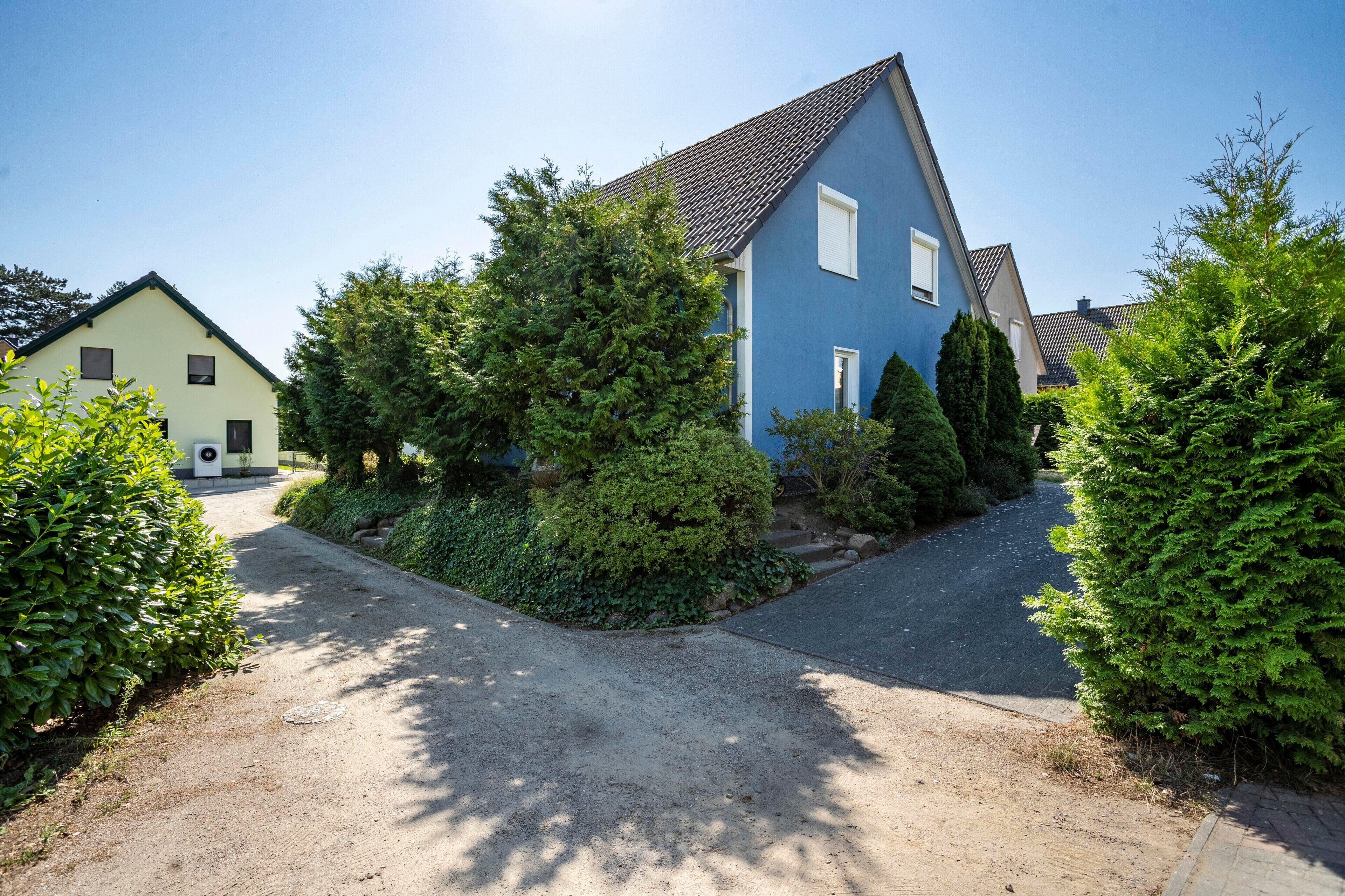 Un quartier résidentiel avec une maison bleue, une allée et de la verdure environnante.
