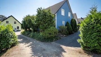 A residential area with a blue house, a driveway, and surrounding greenery.