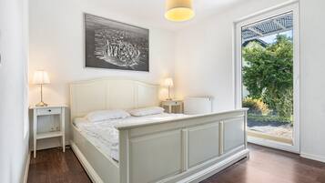 A bedroom with a bed, bedside lamps, a radiator, and a window with a view of greenery.