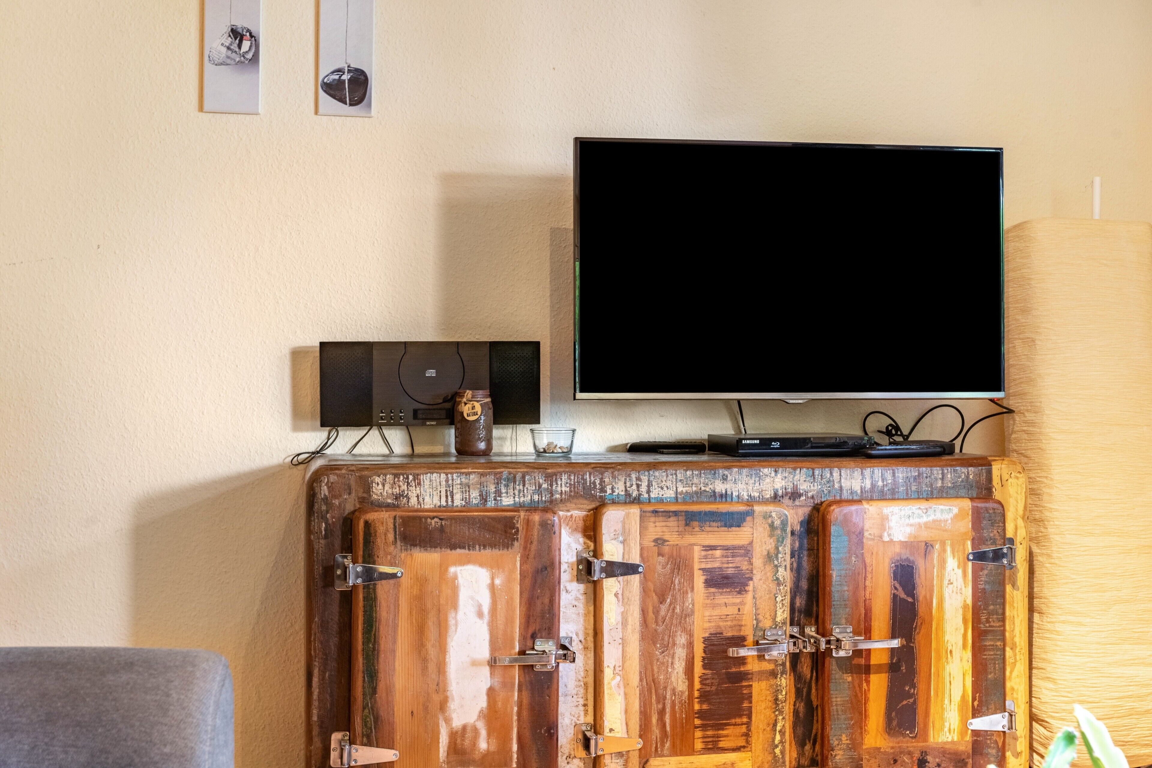 Un televisor sobre un mueble de madera con televisión de pantalla plana, un altavoz y un tarro de miel encima.