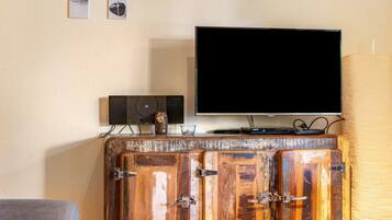 Un televisor sobre un mueble de madera con televisión de pantalla plana, un altavoz y un tarro de miel encima.