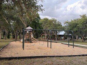 A playground with a slide, swings, and a climbing structure surrounded by trees. - Relaxing Safari Tent with Fire Pit Near Anna Maria Island in Bradenton, Florida (Bradenton)