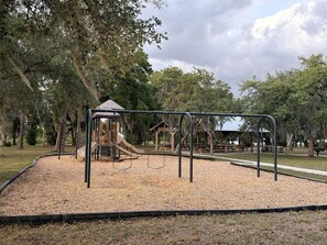 Un parque infantil con tobogán, columpios y una estructura de escalada rodeado de árboles.