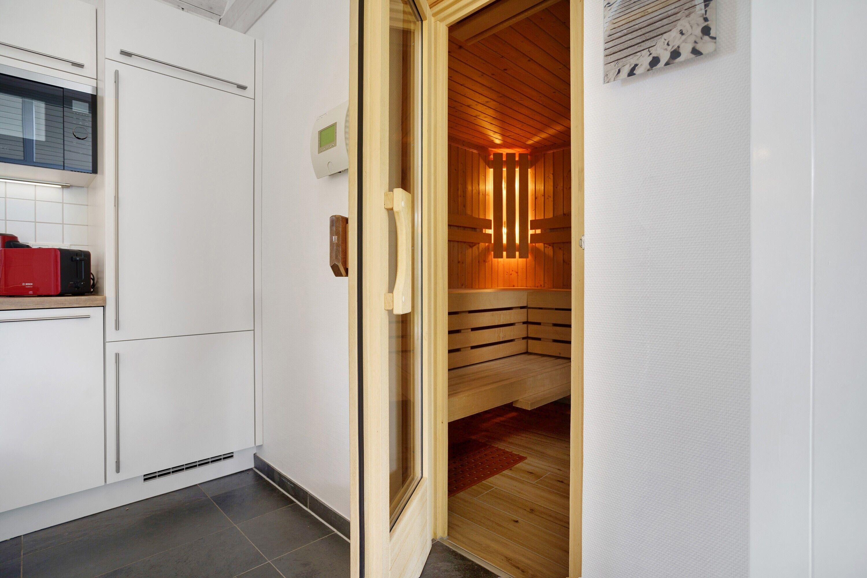Un sauna avec des lambris en bois et une porte en verre donnant sur un espace de salle de bain carrelé.
