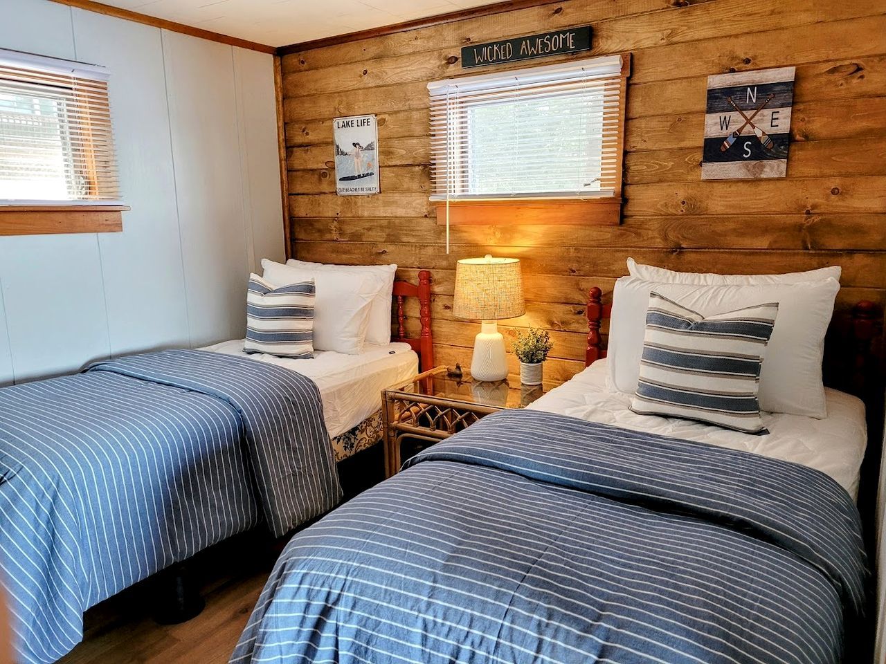 A room with two beds, wooden walls, a sign reading 'WICKED AWESOME,' and a 'LAKE LIFE' poster.