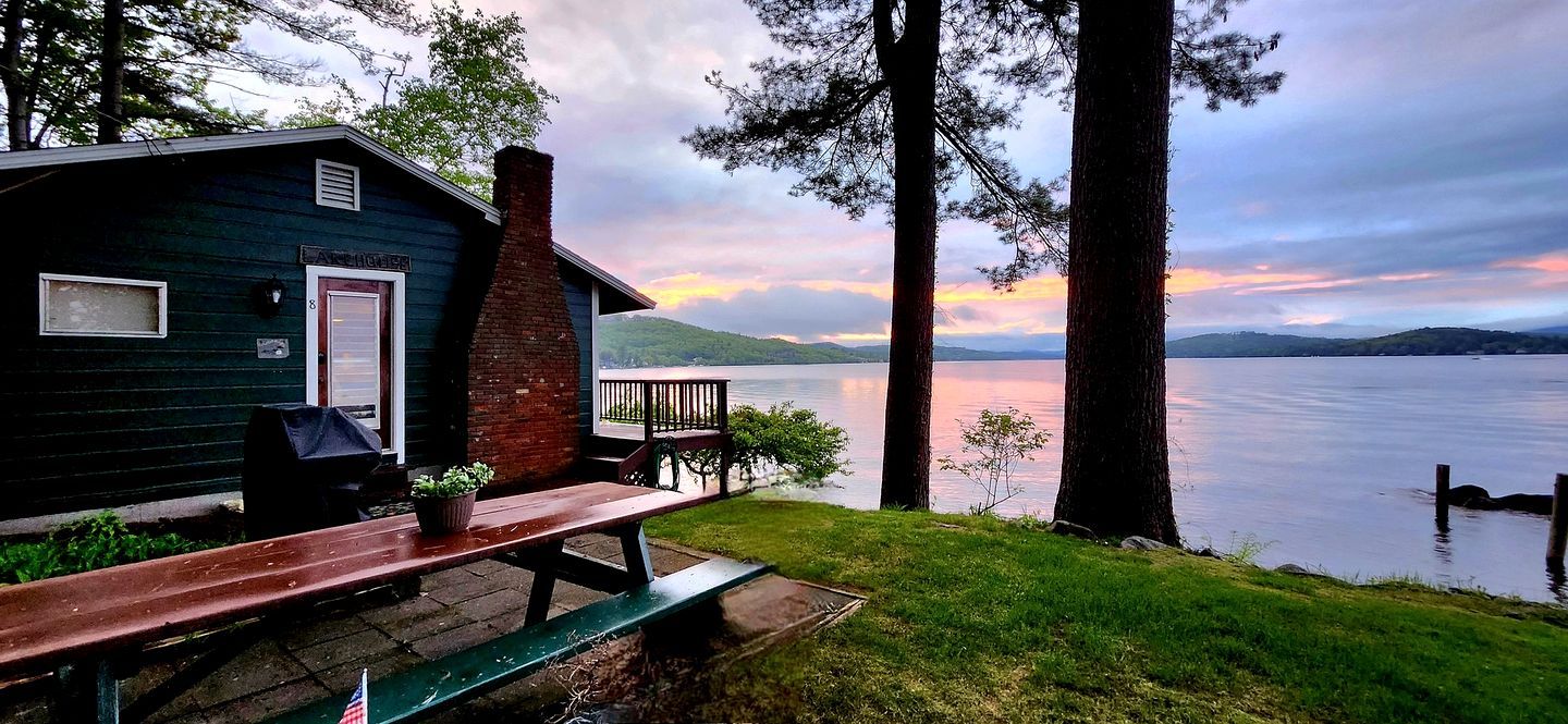 A cabin with a deck overlooking a lake, a picnic table, and a small garden area.