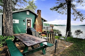 Una cabaña junto al lago con una mesa de picnic y sillas, una chimenea de ladrillo y vistas al lago.