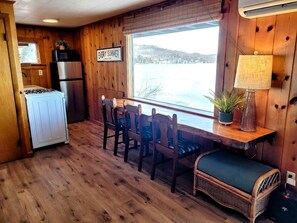 A cabin interior with a kitchen, dining area, and a window overlooking a lake. - Scenic Lakeside Cabin with Exclusive Boat Dock Near Weirs Beach, Laconia, New Hampshire (Laconia)