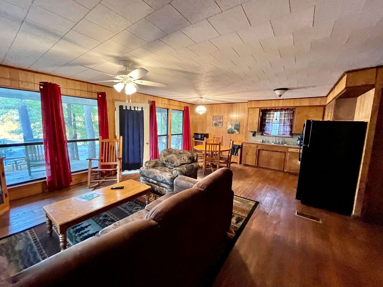 A cozy living room with a sofa, a rocking chair, a dining table, and a kitchen area with a refrigerator.