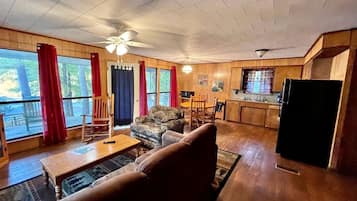 A cozy living room with a sofa, a rocking chair, a dining table, and a kitchen area with a refrigerator.