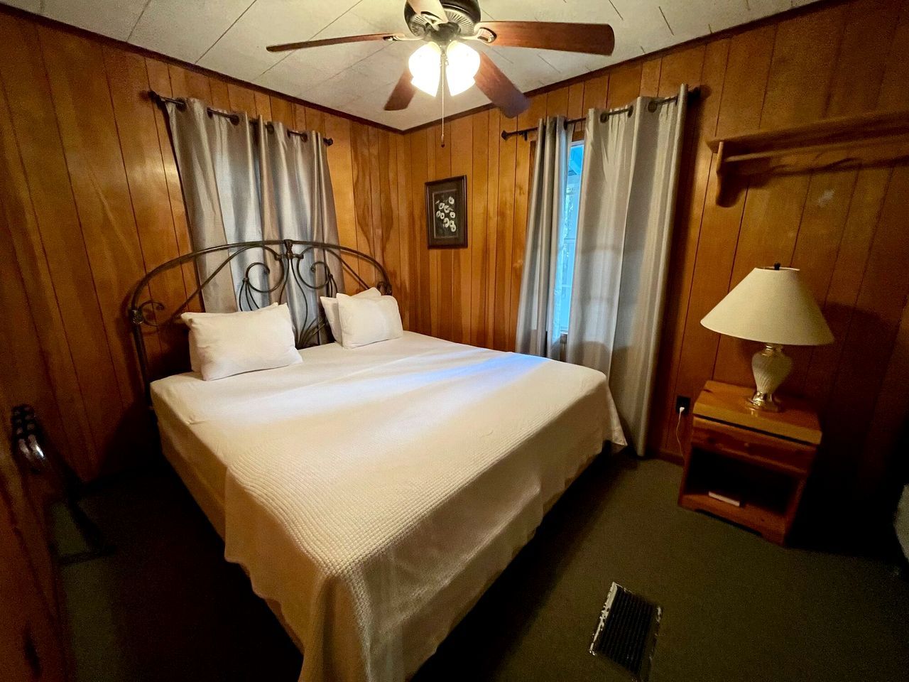 Ein Hotelzimmer mit Bett, Deckenventilator, Holzwänden und einem Nachttisch mit Lampe.
