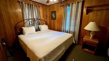 Ein Hotelzimmer mit Bett, Deckenventilator, Holzwänden und einem Nachttisch mit Lampe.