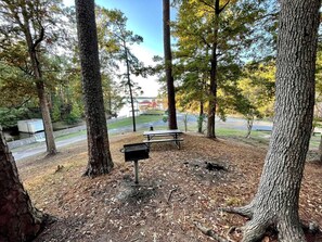A picnic area with a grill, benches, and a view of a body of water and buildings in the background. - Spacious Lakeview Cabin with Fishing Pier Access Near Zwolle, Louisiana (Zwolle)