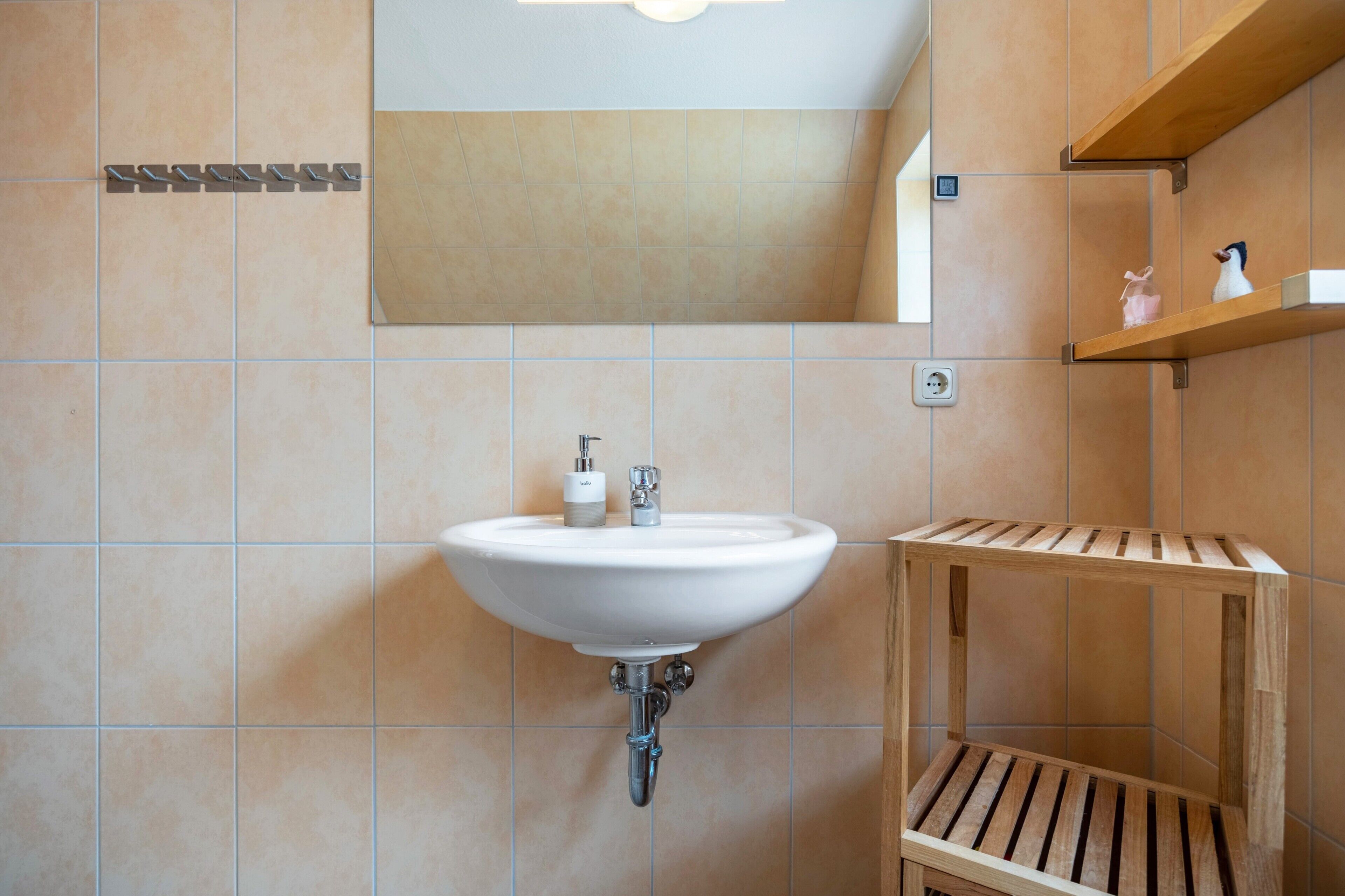Een badkamer met een witte wastafel, een spiegel en houten planken.