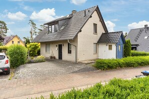 Een woonhuis met twee verdiepingen, een schuin dak, een voordeur en een kleine zij-ingang.