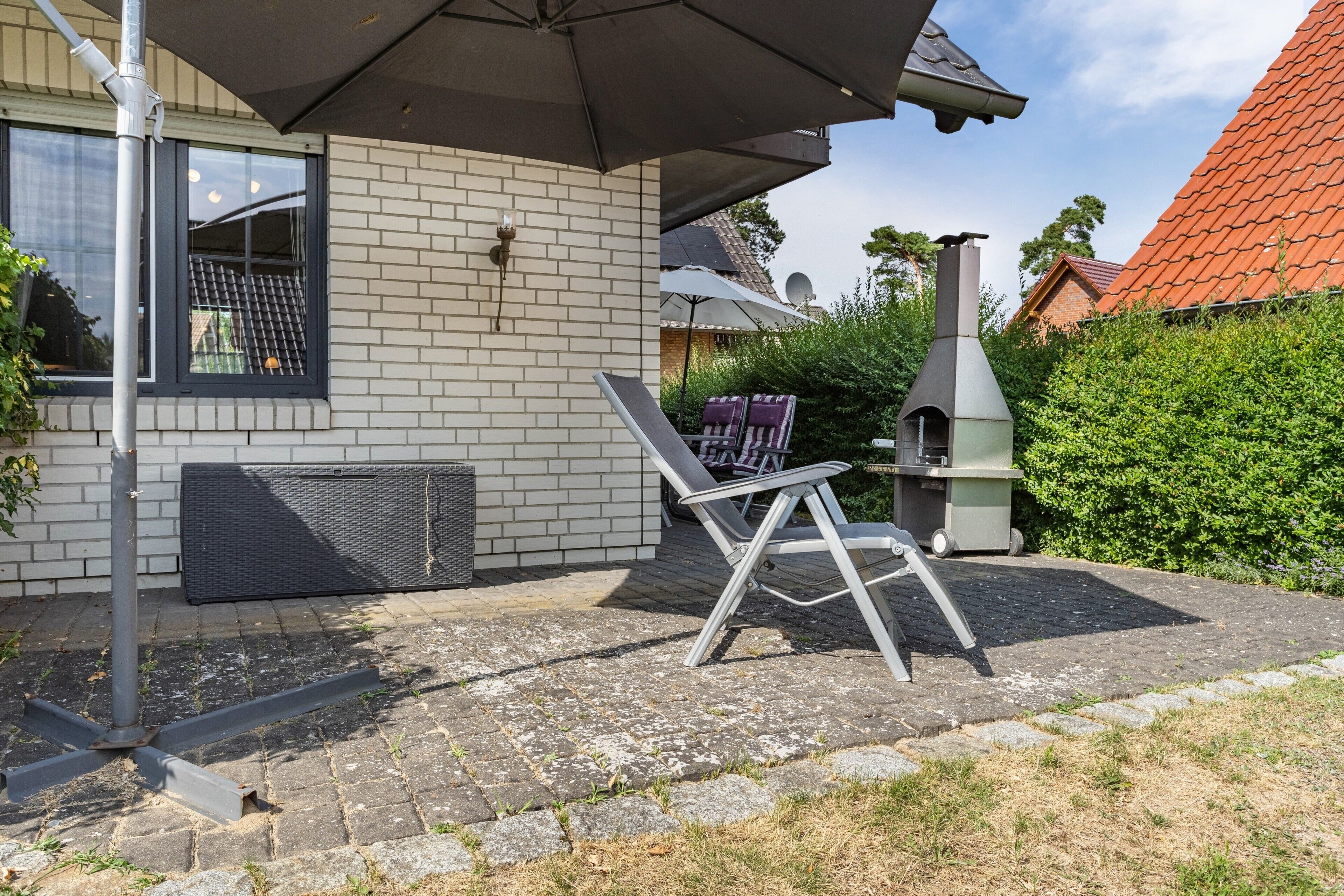 Un espace patio avec un mur en briques, une chaise en métal, un parasol et une cheminée.
