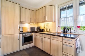 A modern kitchen with wooden cabinets, a built-in oven, a microwave, and a coffee maker. - Apartment 'Haus 28 EG' with Private Terrace, Private Garden and Wi-Fi (Röbel)