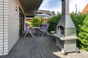 Een terras buiten, met een barbecue, twee opklapbare stoelen en een tafel.