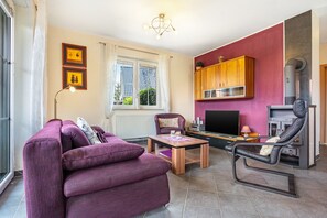 Een woonkamer met een paarse bank, een houten salontafel, een televisie en een open haard.