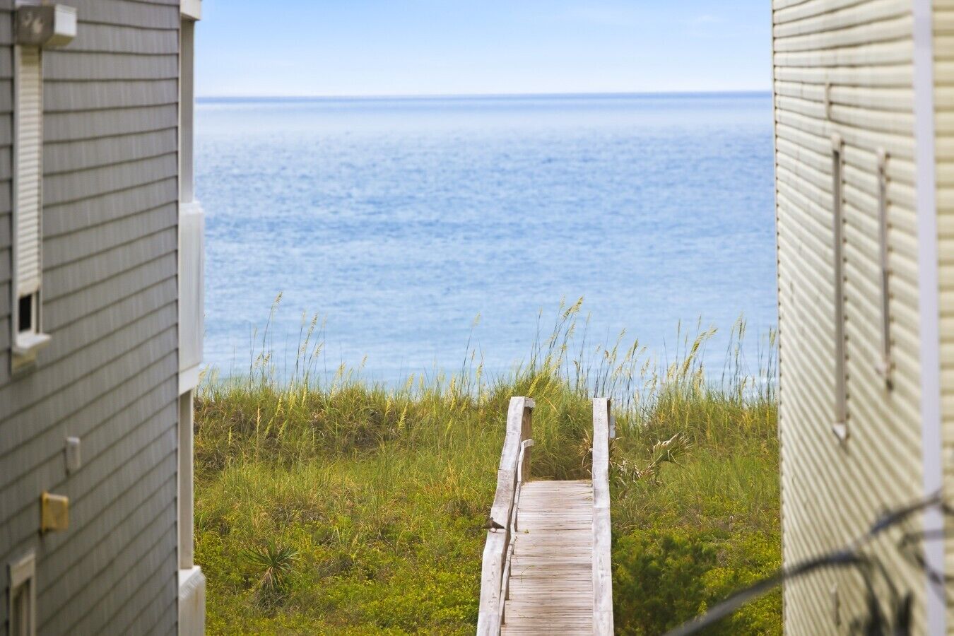 Eine Holzterrasse führt zu einer Wiese mit Blick aufs Meer.