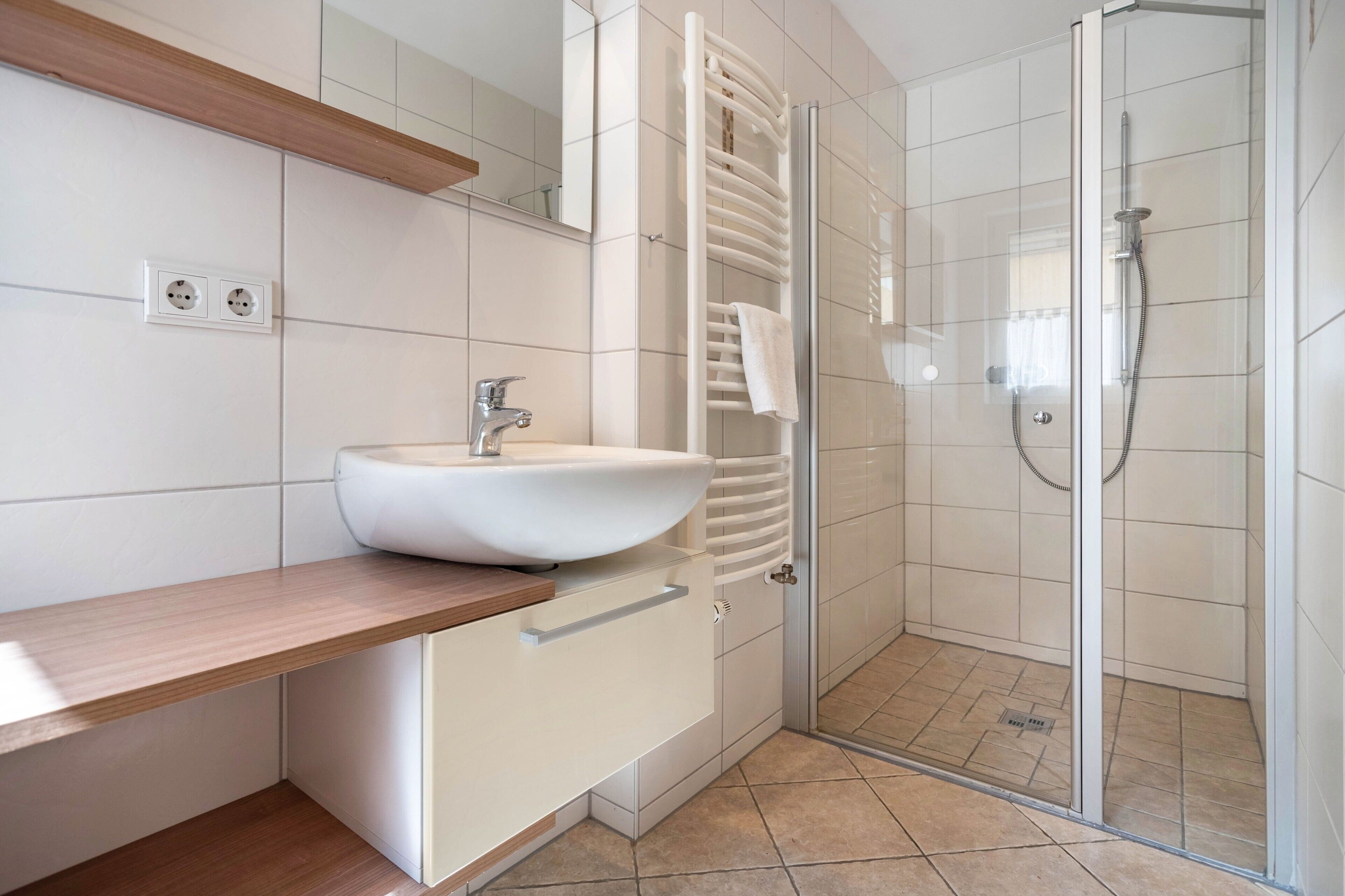 Ein modernes Badezimmer mit einem weißen Waschbecken, einem Holzschrank, einer Glasdusche und einem Handtuchhalter.