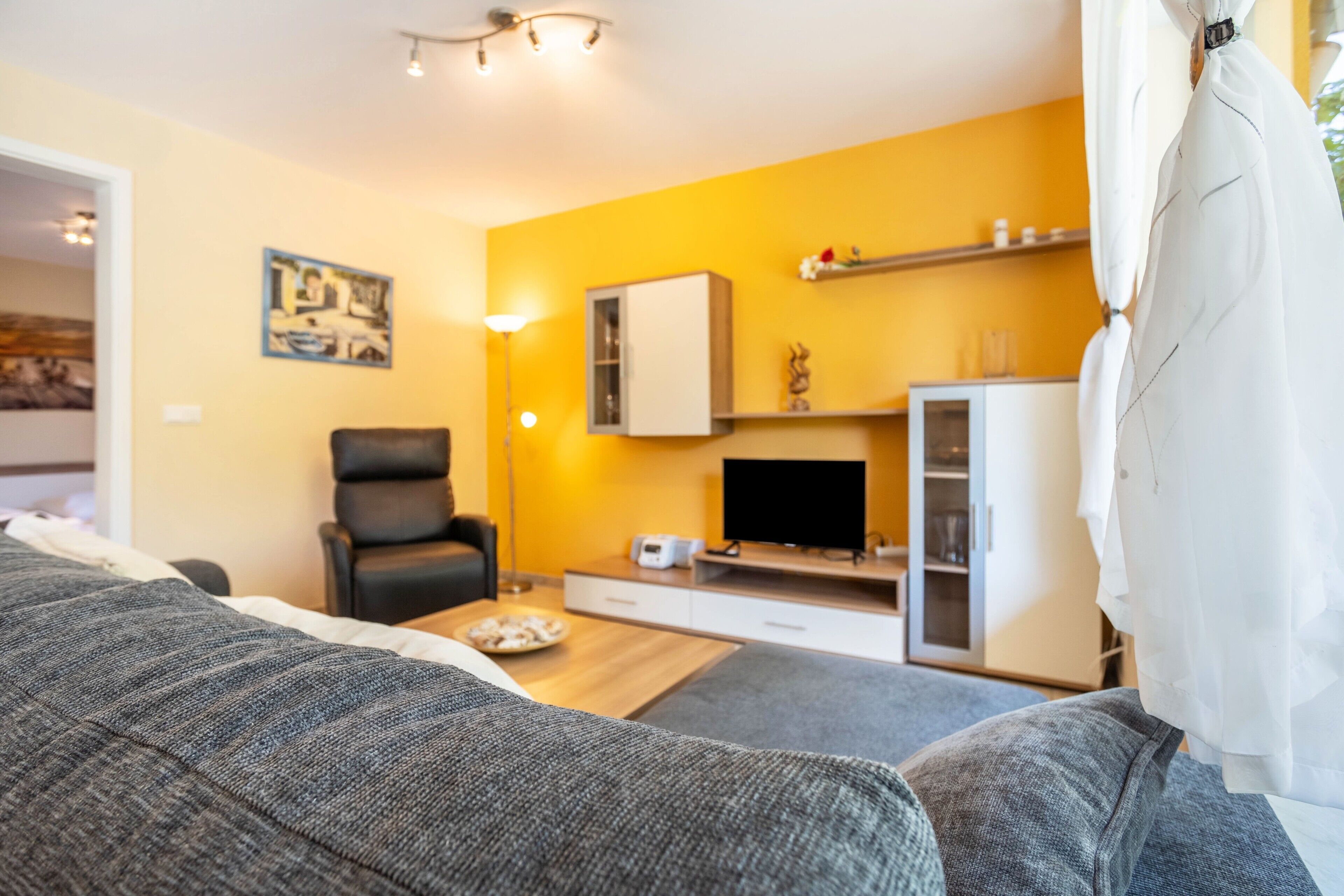 Ein modernes Wohnzimmer mit Sofa, Flachbildfernseher, Stuhl und Essbereich mit Tisch und einem Teller Essen.