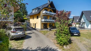 A residential building with a two-story structure, a visible balcony, and a paved driveway.