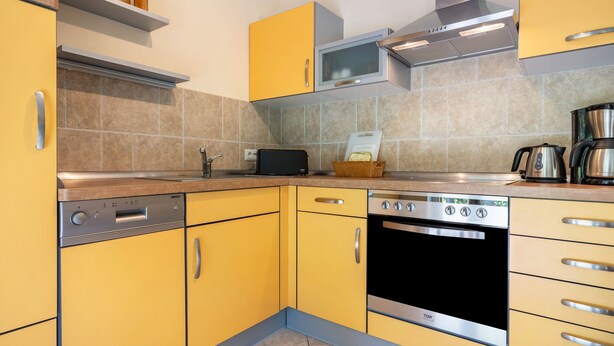 A kitchen with yellow cabinets, a built-in oven, a microwave, and a coffee maker.