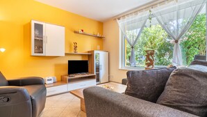 A living room with a sofa, a television, a cabinet, and a window with a view of greenery.