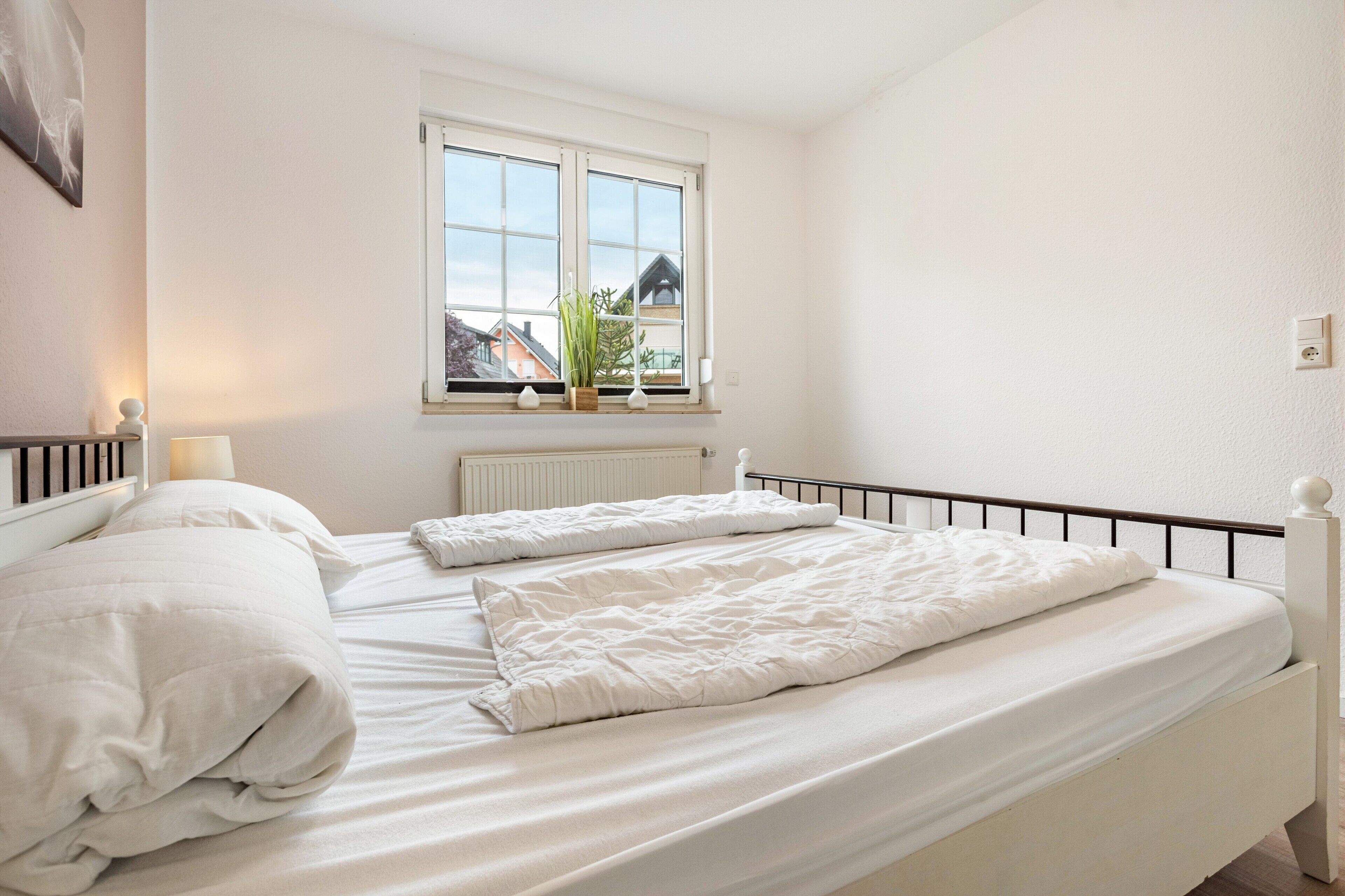 Ein Schlafzimmer mit einem Bett, einem Fenster, einem Heizkörper und einer Pflanze auf der Fensterbank.