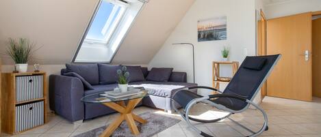 Een moderne woonkamer met een schuine kap, een bank, een glazen salontafel, een schommelstoel en een dakraam.