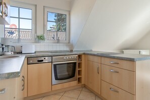 A kitchen with a Bosch dishwasher, a built-in oven, wooden cabinets, and a window with a view of the outside. - Apartment 'Haus 7 OG' with Lake View, Private Garden and Wi-Fi (Röbel)