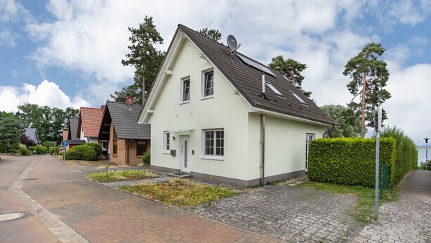A two-story house with a sloped roof, satellite dish, and a small front yard with a hedge. - Apartment 'Haus 7 OG' with Lake View, Private Garden and Wi-Fi (Röbel)