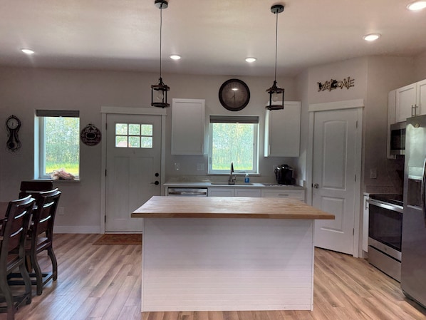 A kitchen with a central island, wooden flooring, white cabinetry, a stainless steel refrigerator, and a clock on the wall.