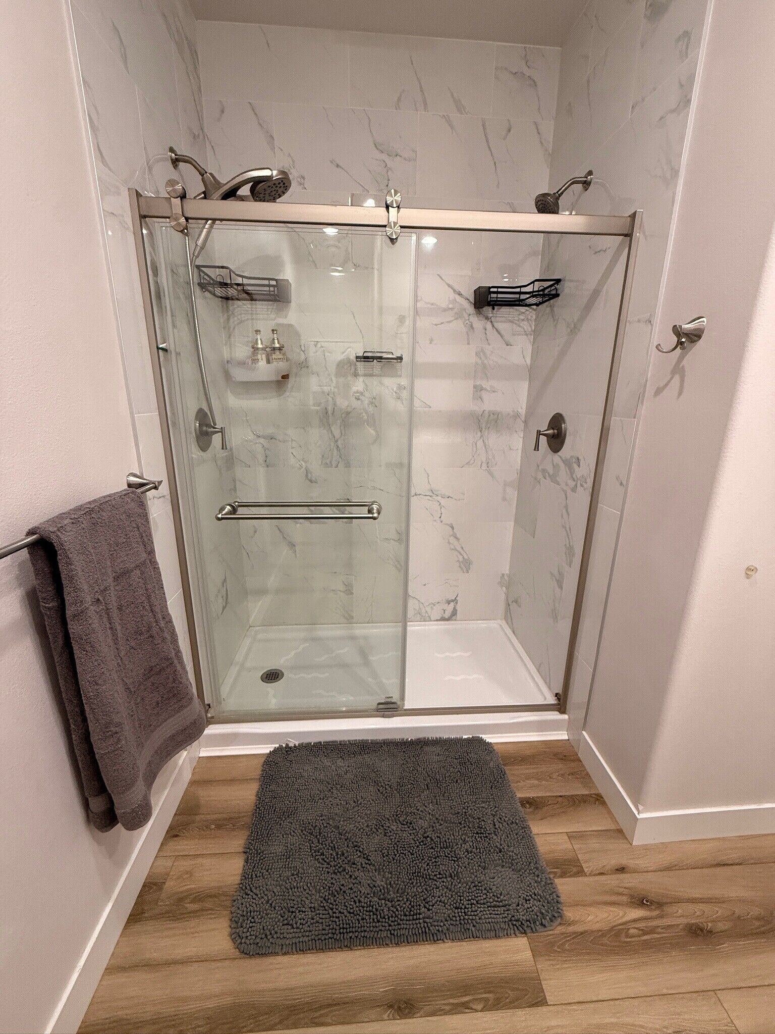En dusch med glasväggar, en handduksställning och en mörk matta på golvet.