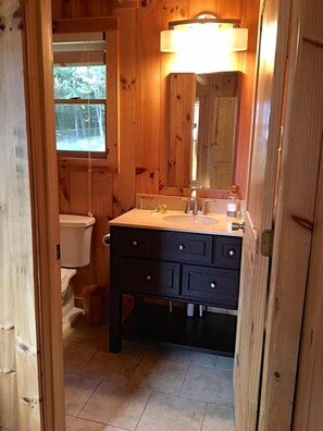 Et badeværelse i træ med vask, spejl og toilet.
