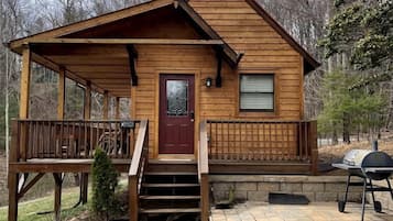 A wooden cabin with a front porch, a red door, and a grill outside.