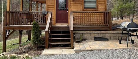 A wooden cabin with a front porch, a red door, and a grill outside.