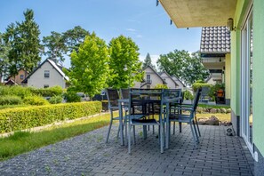 A patio with a table and chairs, a paved walkway, and a hedge. - Apartment 'Haus U13 EG' with Private Garden, Balcony and Wi-Fi (Röbel)