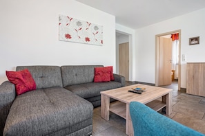 Ein Wohnzimmer mit grauem Sofa, roten Kissen, einem Holztisch und einem blauen Sessel.
