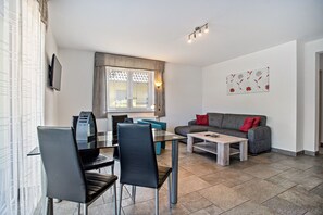 A modern living room with a dining area, grey sofa, and a flat-screen TV mounted on the wall. - Apartment 'Haus U13 EG' with Private Garden, Balcony and Wi-Fi (Röbel)