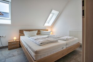 A bedroom with a sloped ceiling, a bed with white bedding, a bedside table with a lamp, and a window with a view of the roof. - Apartment 'Haus U13 OG' with Private Terrace, Private Garden and Wi-Fi (Röbel)