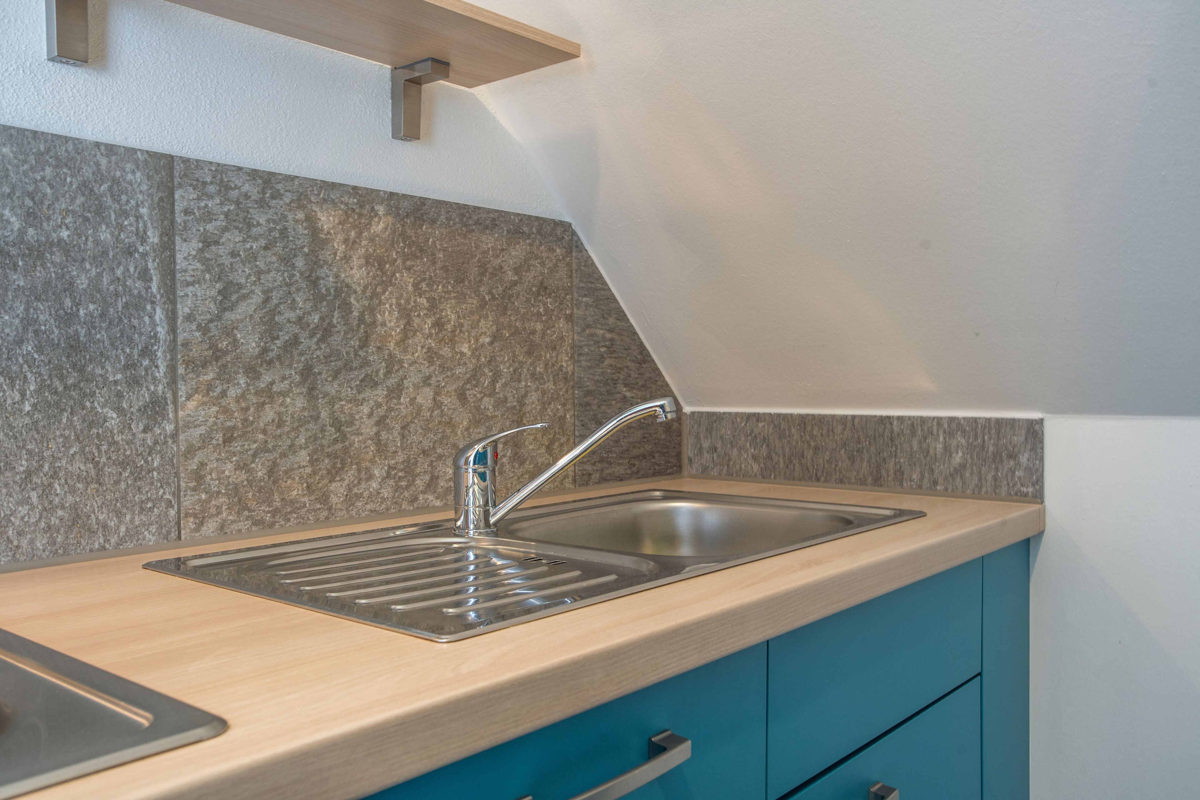 Una cocina con un lavamanos de acero inoxidable, encimera de madera y armarios color turquesa.