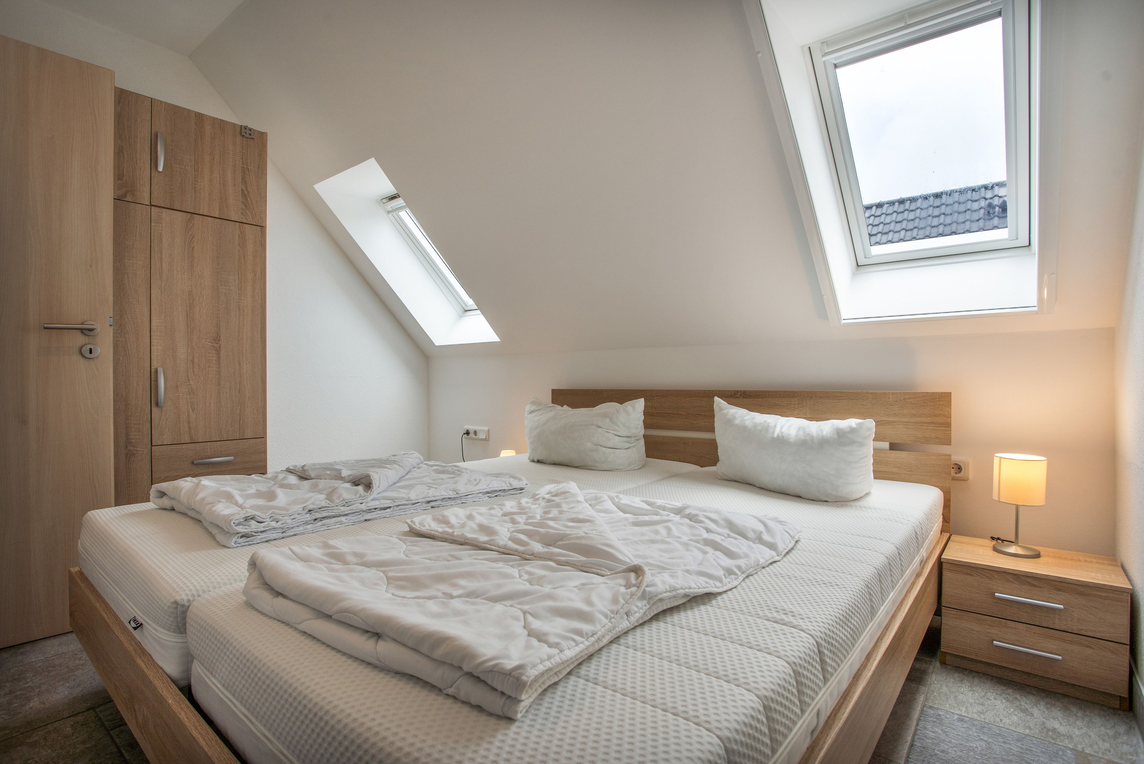 Une chambre à coucher avec un lit, une table de chevet, une lampe, une armoire et un puits de lumière.