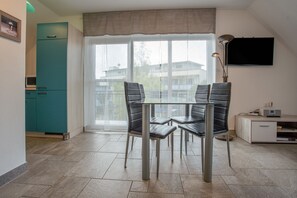 Una cocina moderna con armarios color turquesa, una mesa de comedor de vidrio con cuatro sillas y un ventanal con vistas a edificios.