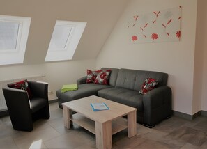 Una sala de estar con un sofá gris, un sillón negro, una mesa de centro de madera y una pared decorada con una obra de arte floral.