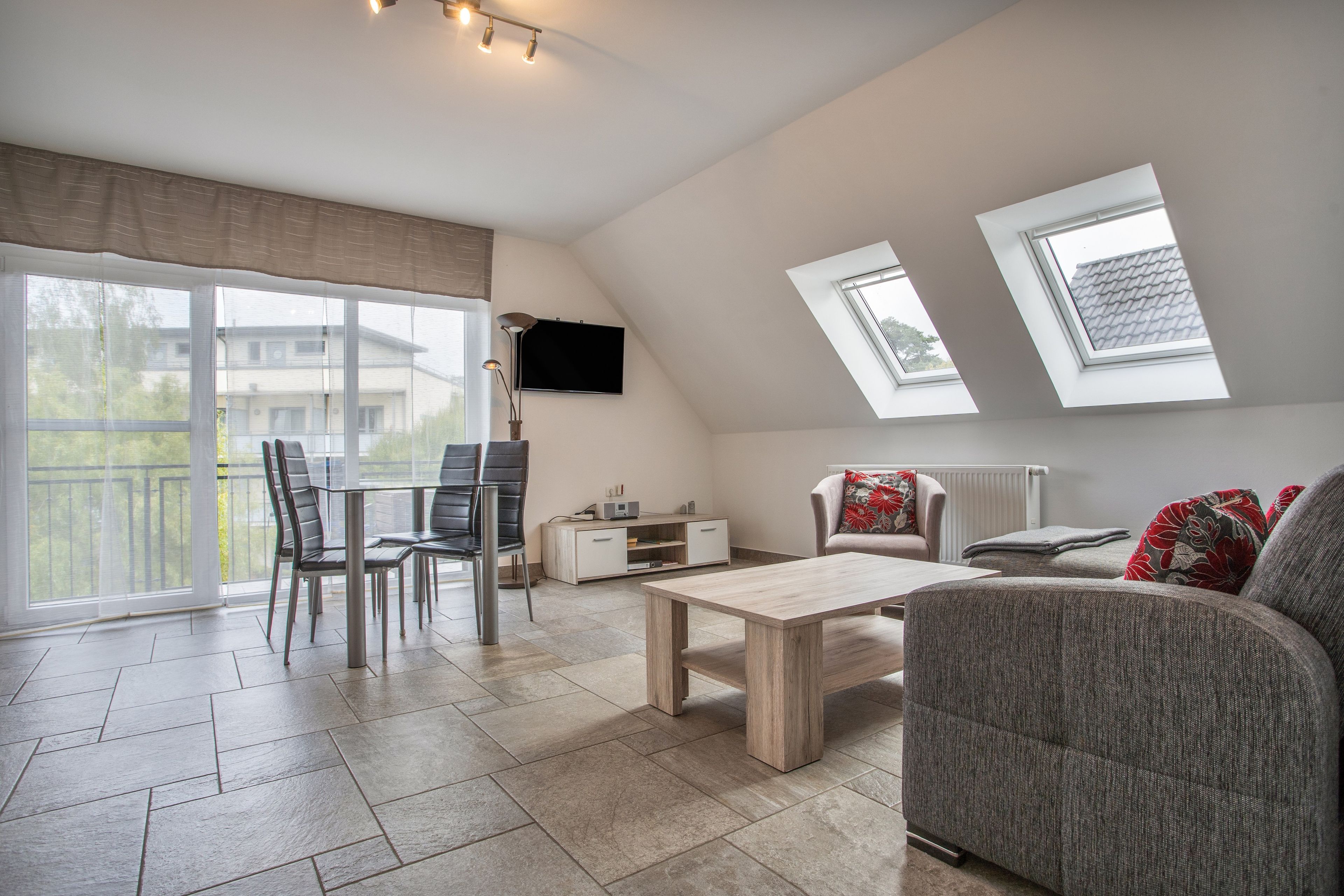 Un salon moderne comprenant un coin repas, un téléviseur à écran plat fixé au mur et un canapé agrémenté de coussins décoratifs.