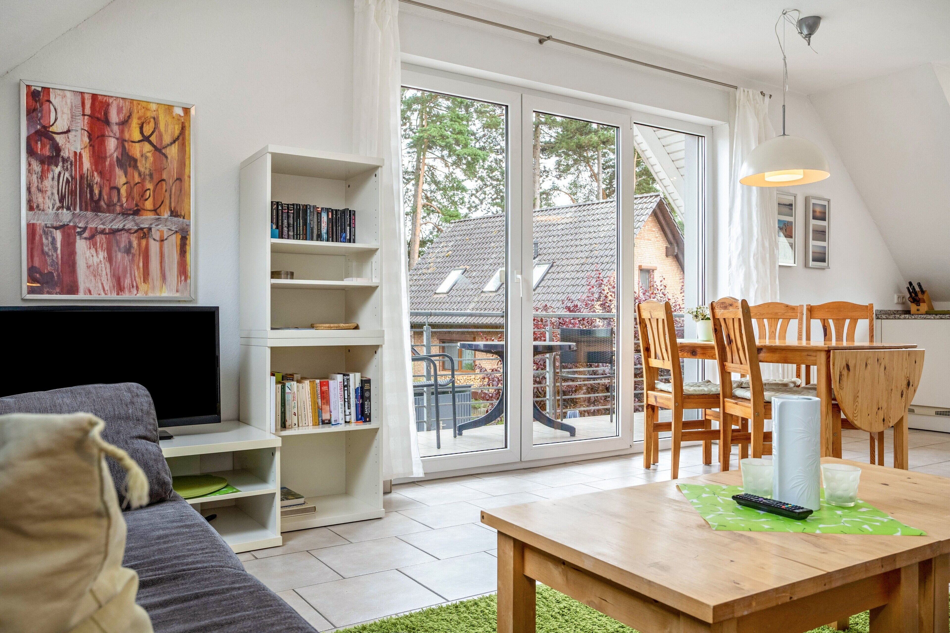 Een moderne woonkamer met een bank, een houten eettafel, een boekenkast en een groot raam.