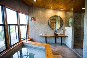 Ein modernes Badezimmer mit großem Fenster, rundem Spiegel, Holzwaschtisch und einer Duschkabine aus Glas.